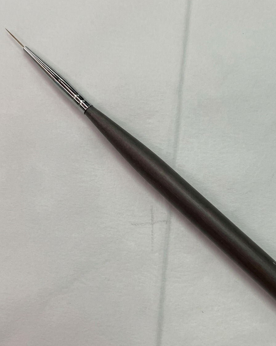 Un pincel delineador fino de nail art posicionado cerca de un boceto de cuadrícula guía clara en una uña de práctica.
