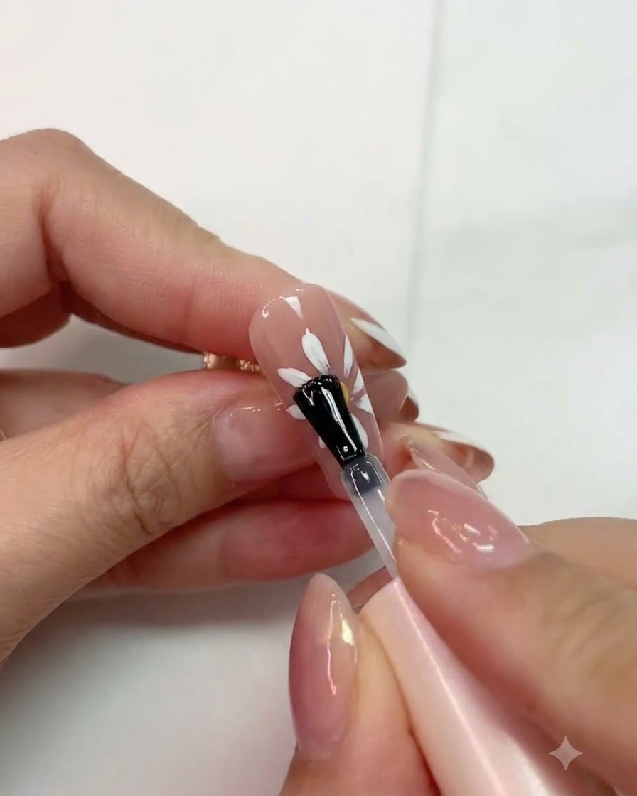 Un pincel aplicando top coat mate sobre un diseño de margarita blanca curada en una uña rosa.