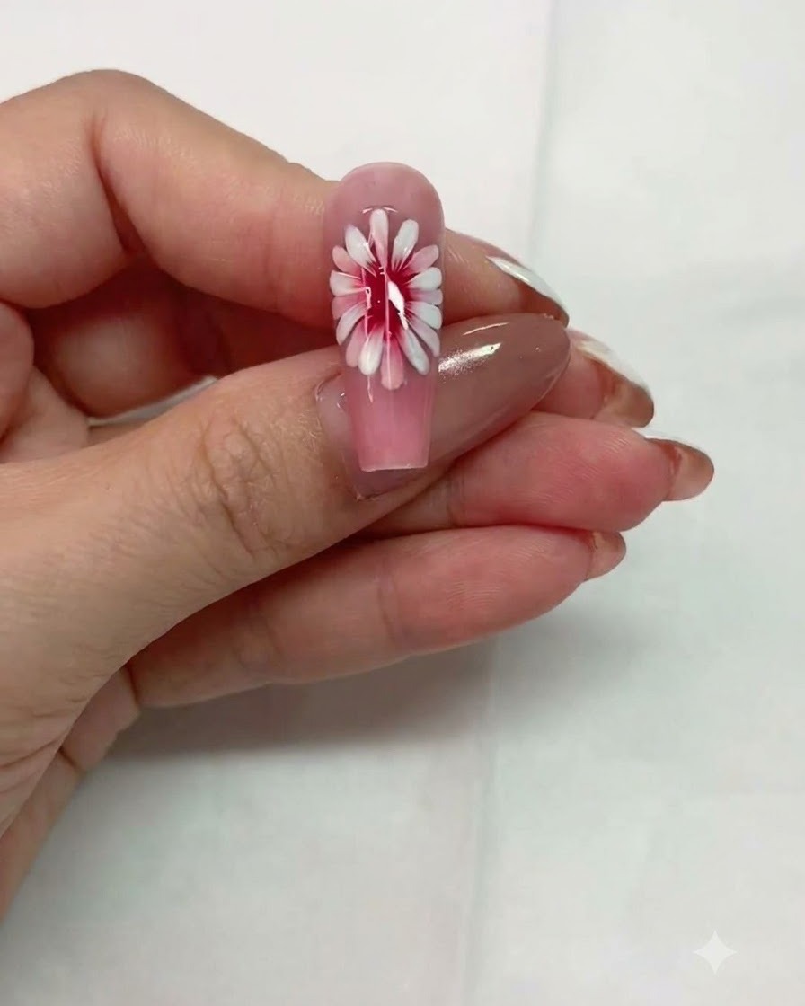 Una vista de cerca de una uña rosa con un diseño de margarita de múltiples capas reposando antes de curar.