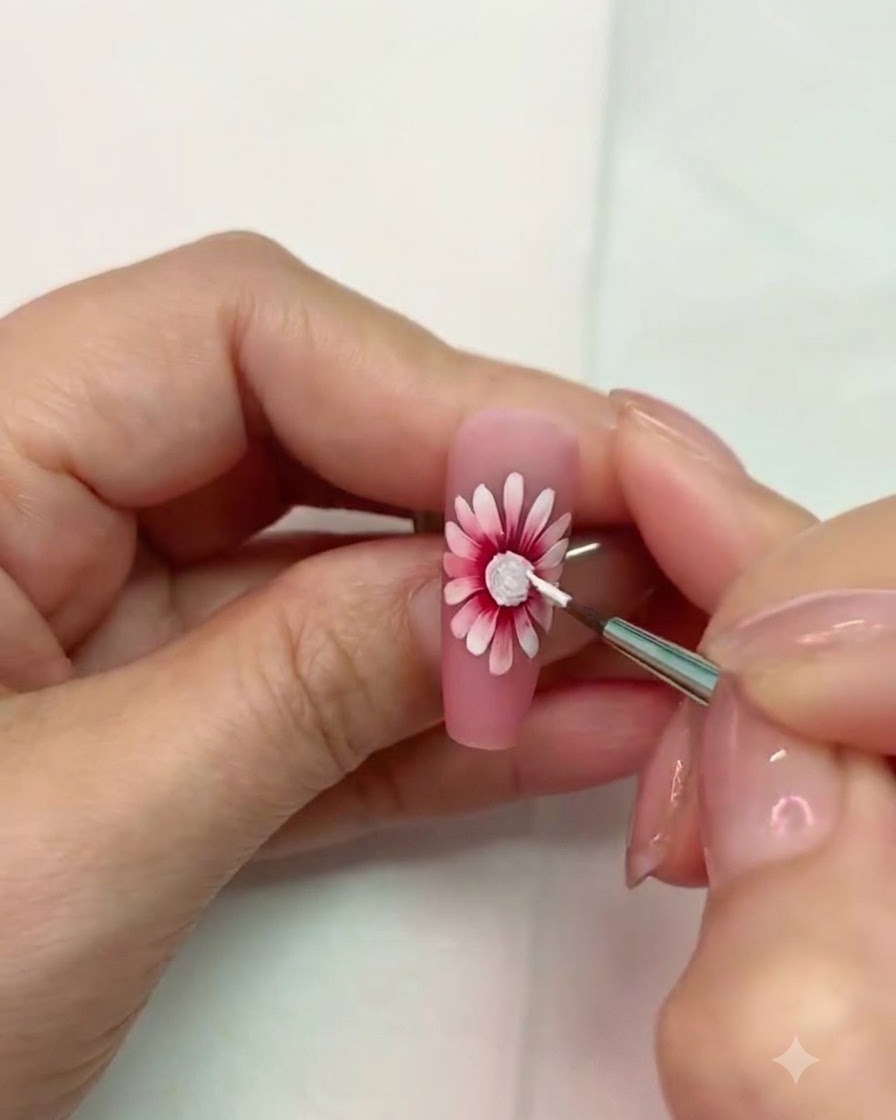 Un pincel fino trabajando cerca del centro texturizado blanco curado del arte de uñas de margarita.