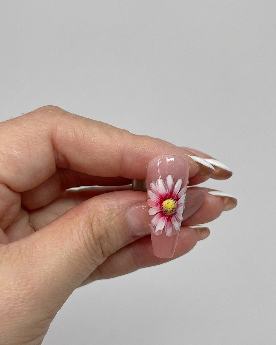 Un pincel aplicando un top coat brillante sobre un diseño de uña de margarita de doble capa terminado.