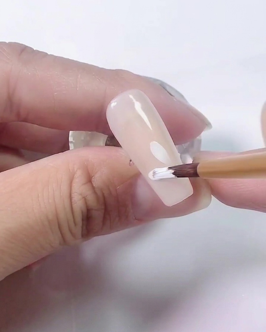 Una vista cercana de un pincel añadiendo más pétalos al diseño de la margarita blanca sobre una base nude.
