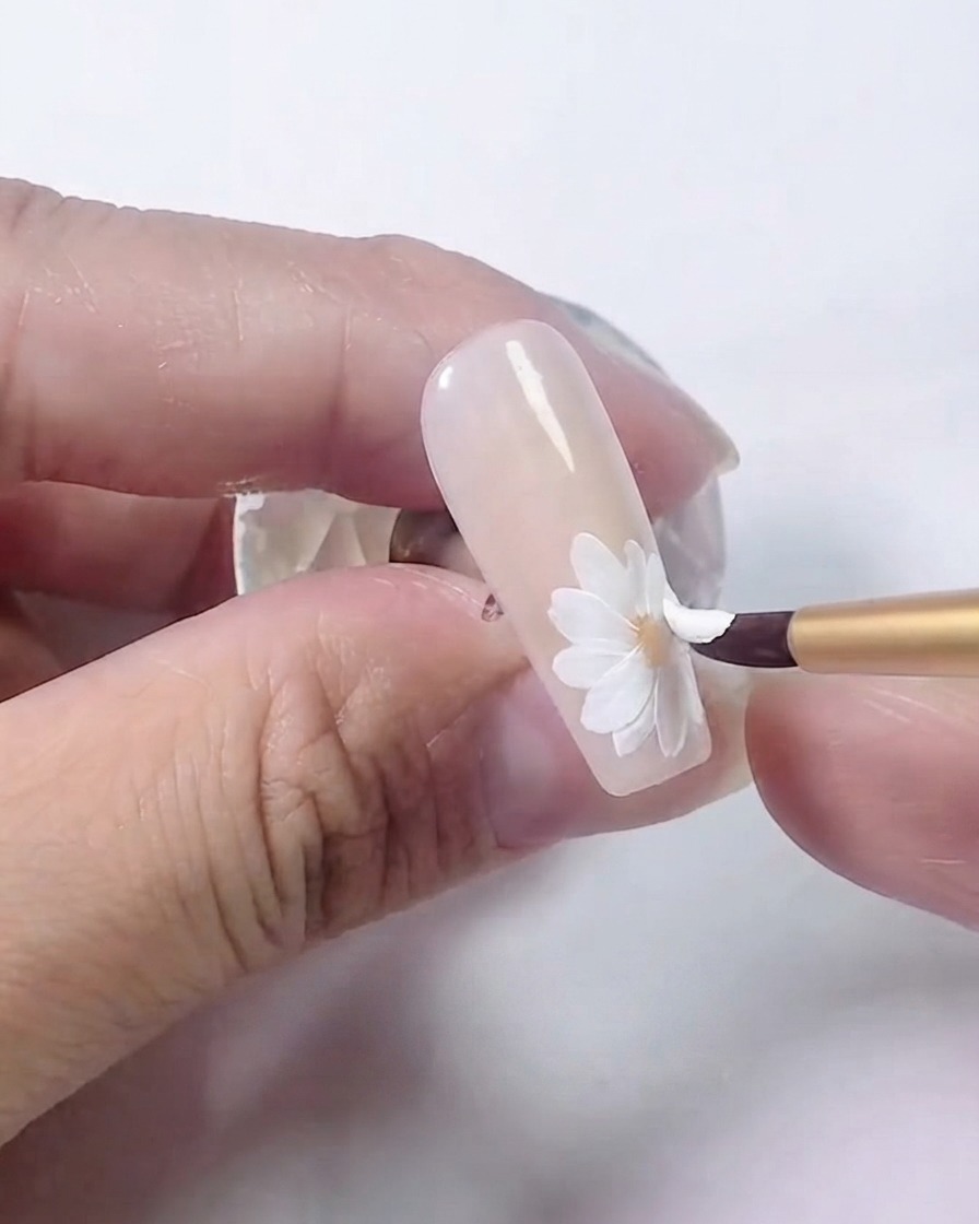 Un pincel de uñas añadiendo una segunda capa superpuesta de pétalos blancos sobre la margarita.