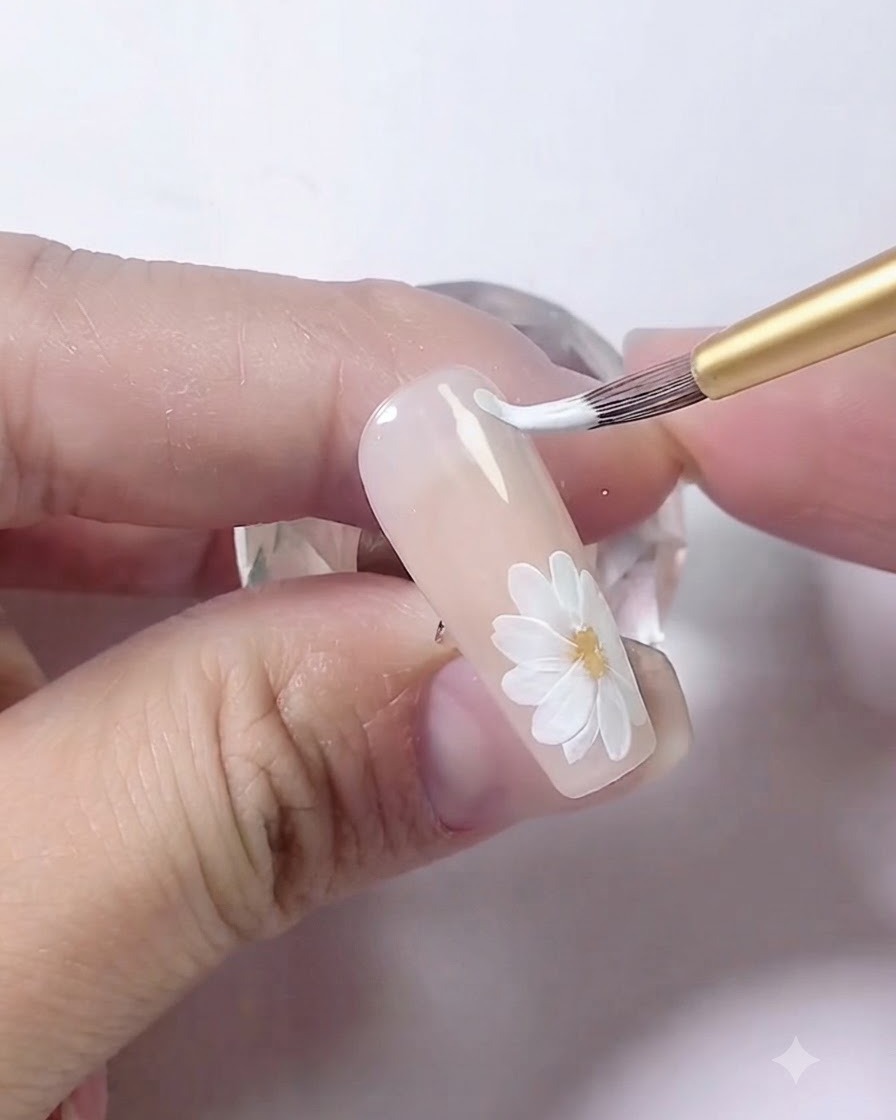 Un pincel de arte en uñas dibujando dos líneas blancas paralelas curvadas a lo largo del borde de la uña.