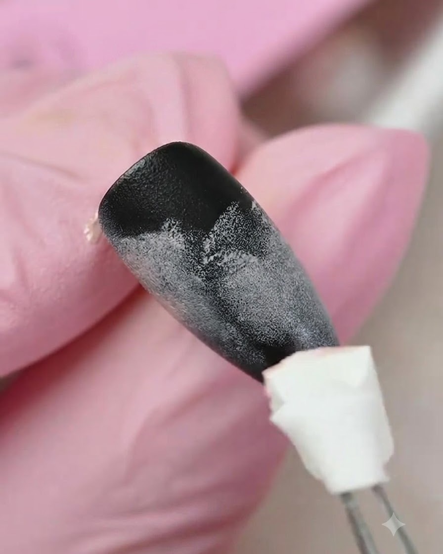 Un aplicador de esponja aplicando gel amarillo en la porción inferior de una uña con textura degradada en negro y rosa.