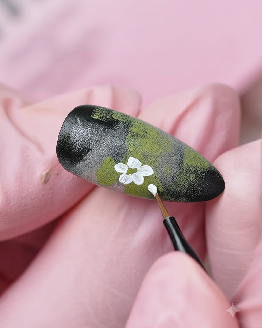 Un pincel delineador fino añadiendo más detalles de flores blancas y brotes sobre el diseño de uñas texturizado.