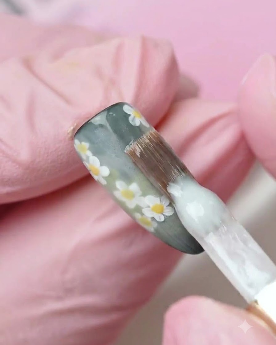 Un pincel aplicando una capa de esmalte en gel blanco lechoso sobre una superficie de uña decorada.