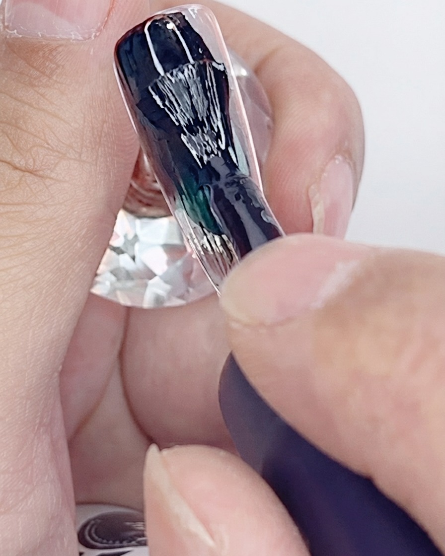 Un pincel aplicando la primera capa de esmalte en gel negro sobre la superficie de una uña artificial.