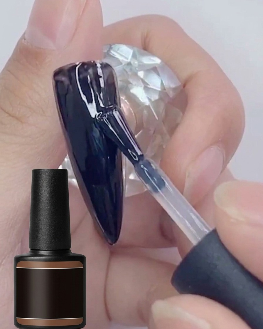 Un pincel aplicando una segunda capa de esmalte en gel negro brillante sobre una superficie de uña pintada de negro.