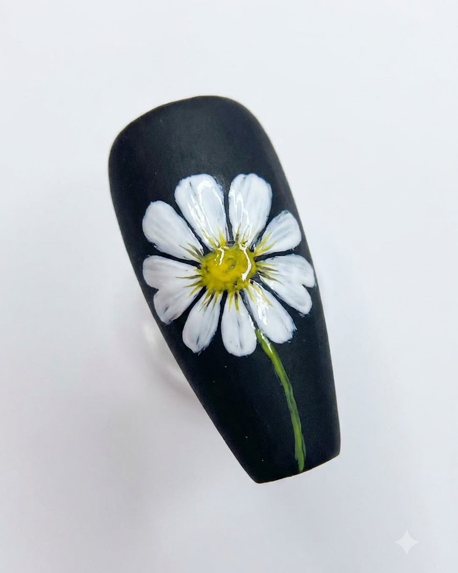 Un diseño de arte en uñas negro completado que muestra una margarita blanca detallada con un centro amarillo brillante y un tallo verde.