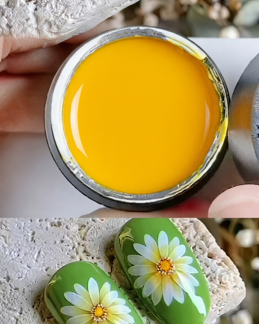 Un primer plano de un pincel fino depositando un punto de gel amarillo en el centro de una margarita pintada.