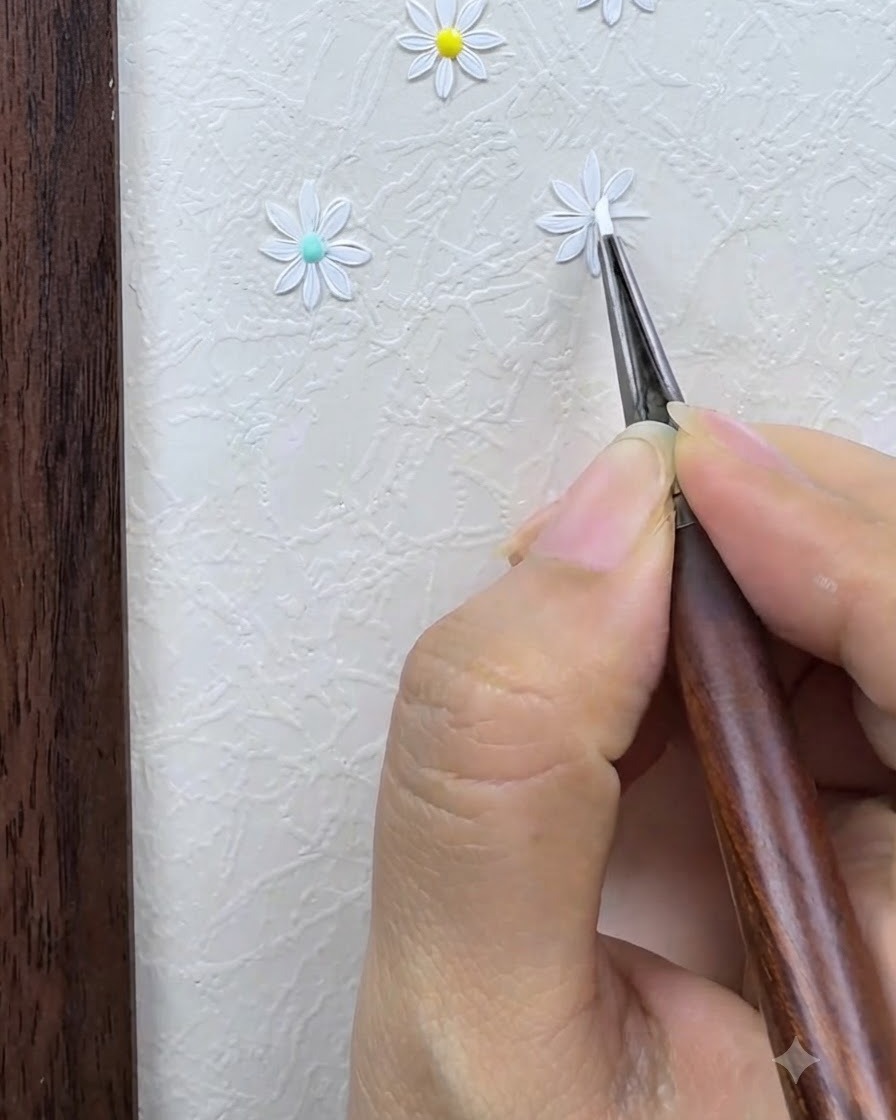 Un pincel de detalle delineando y refinando cuidadosamente los pétalos blancos de una margarita pintada sobre un fondo de nail art texturizado.