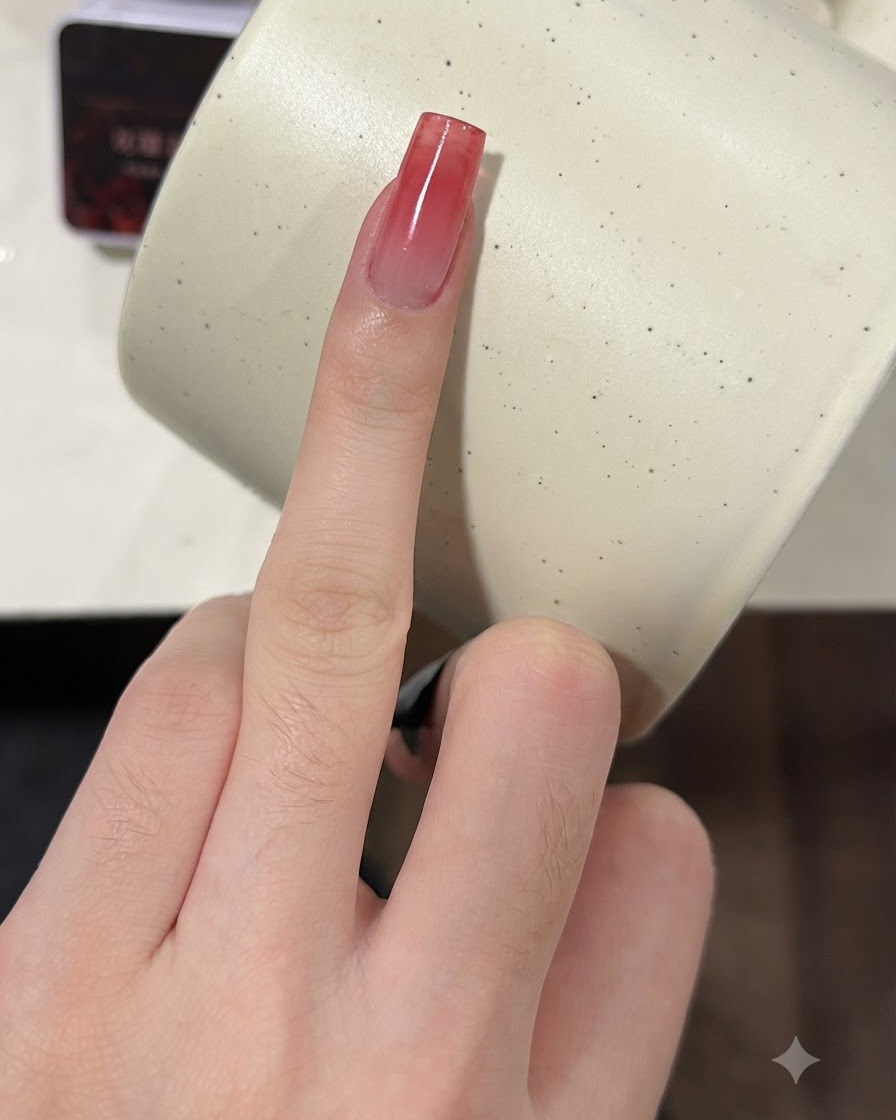 Un dedo con una uña degradada en rojo vino siendo presionada con una esponja para una segunda capa.