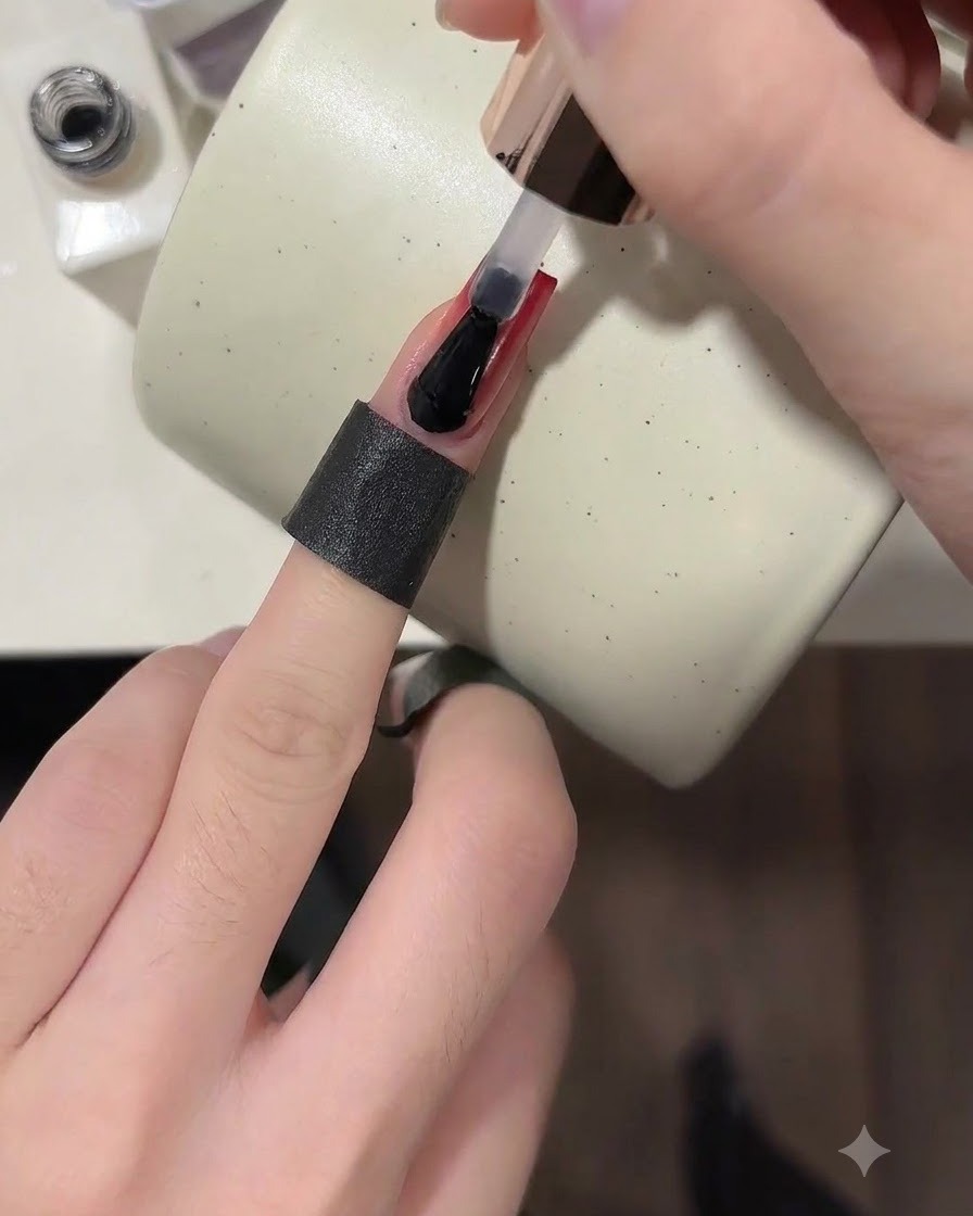 Un pincel aplicando un top coat transparente y brillante sobre una uña degradada en rojo vino terminada.