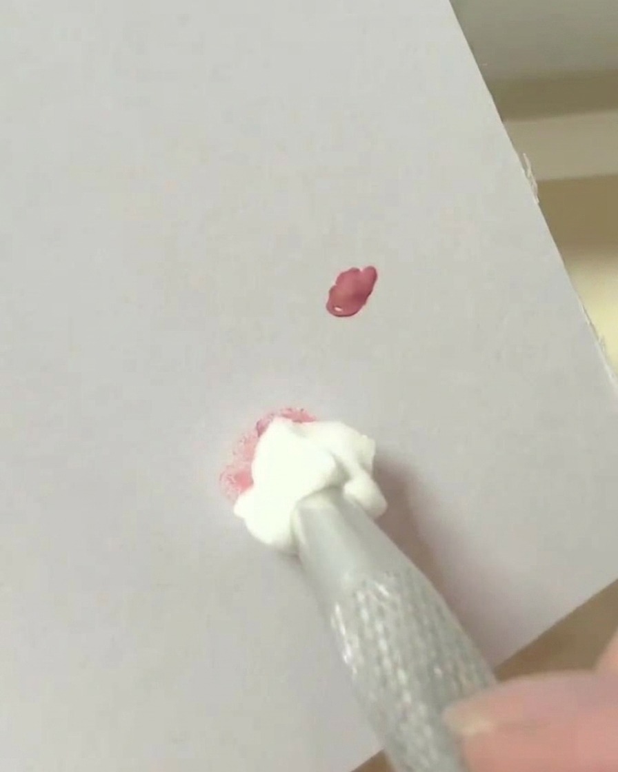 Una herramienta de esponja de maquillaje dando toques en un punto de pigmento mezclado sobre una superficie de paleta blanca.