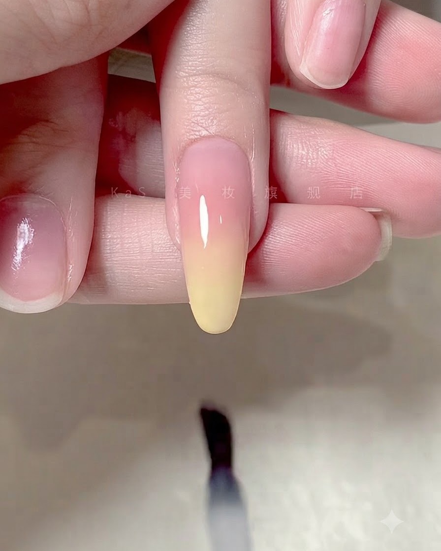 Un pincel aplicando una capa superior transparente y brillante sobre un diseño de uñas con degradado ombré.