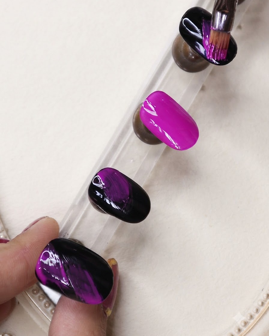 Un pincel delineador fino aplicando rayas de gel negro sobre una uña morado neón vibrante en un soporte de exhibición.