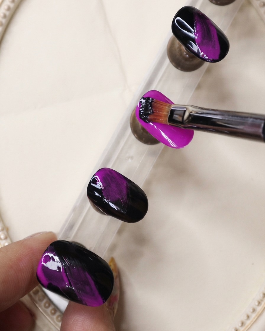 Un pincel delineador fino aplicando gel negro en trazos texturizados sobre una uña morado neón.