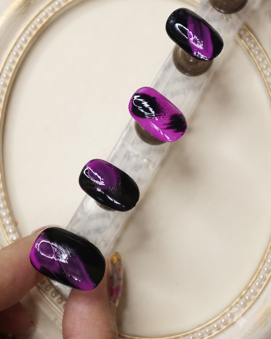 Un pincel de top coat aplicando una capa protectora sobre los diseños de uñas texturizados en negro y morado neón.