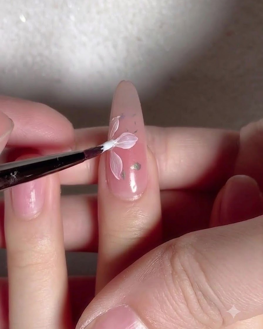 Un pincel aplicando una capa de top coat transparente y brillante sobre una uña decorada con flores y copos.
