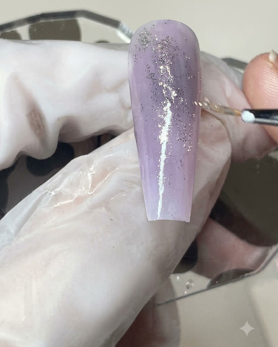 Un pincel de gel aplicando una capa uniforme de acabado mate sobre una uña con degradado morado e incrustaciones de brillo.