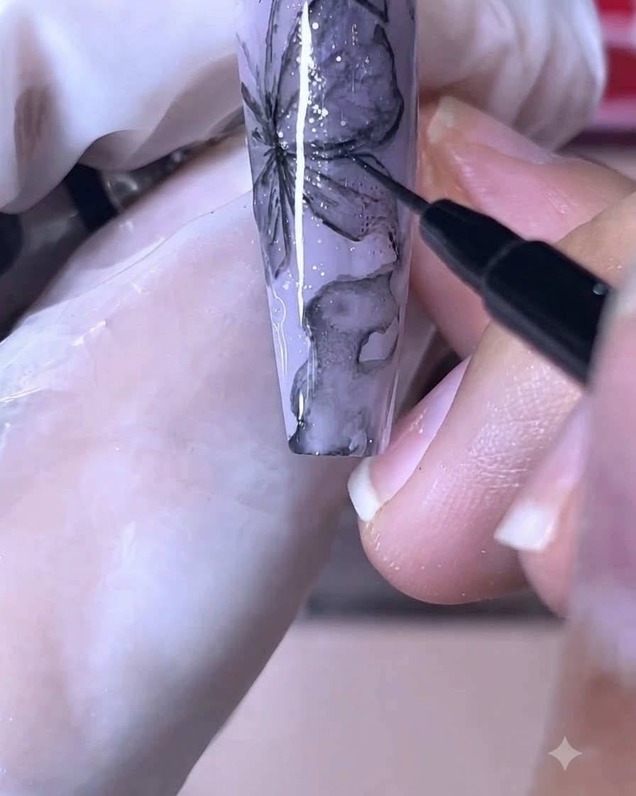 Un pincel de uñas fino dibujando líneas negras nítidas sobre un diseño de uña de mariposa morada.
