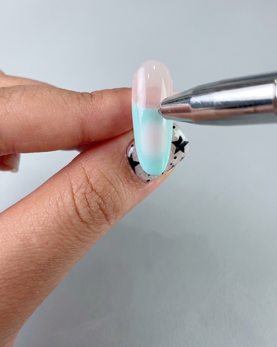 Un aplicador de esponja aplicando un suave degradado blush central con gel suave sobre la uña.