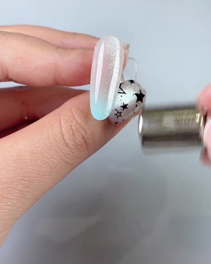 Una varita magnética sostenida cerca del lateral de una uña para atraer y dar forma a una banda de luz cat eye ancha.