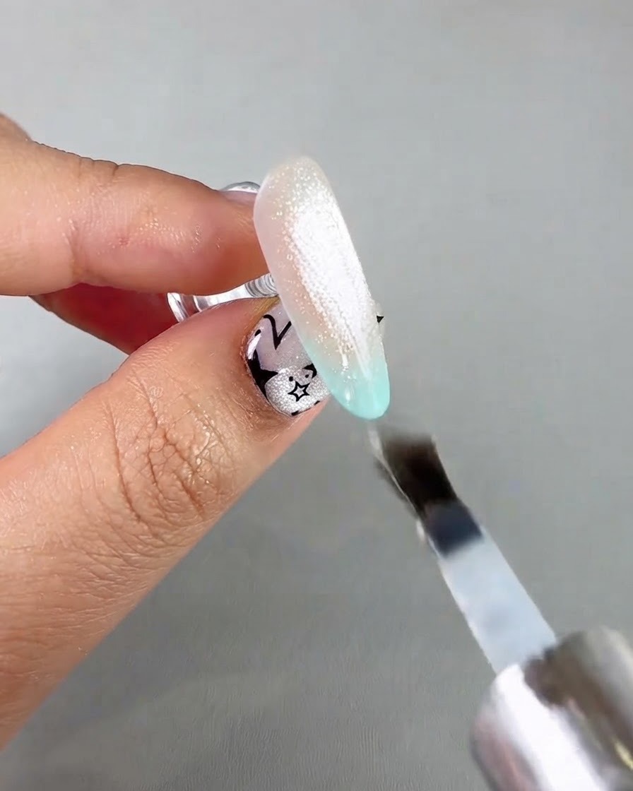 Un pincel de uñas aplicando una capa superior selladora transparente sobre una extensión de uña cat eye brillante.