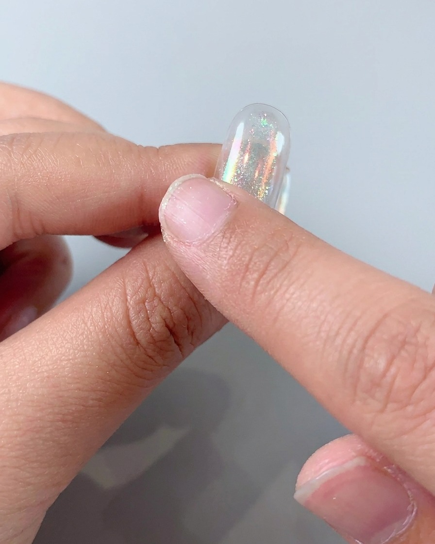 Frotando polvo aurora holográfico sobre una uña para crear un acabado metálico brillante.