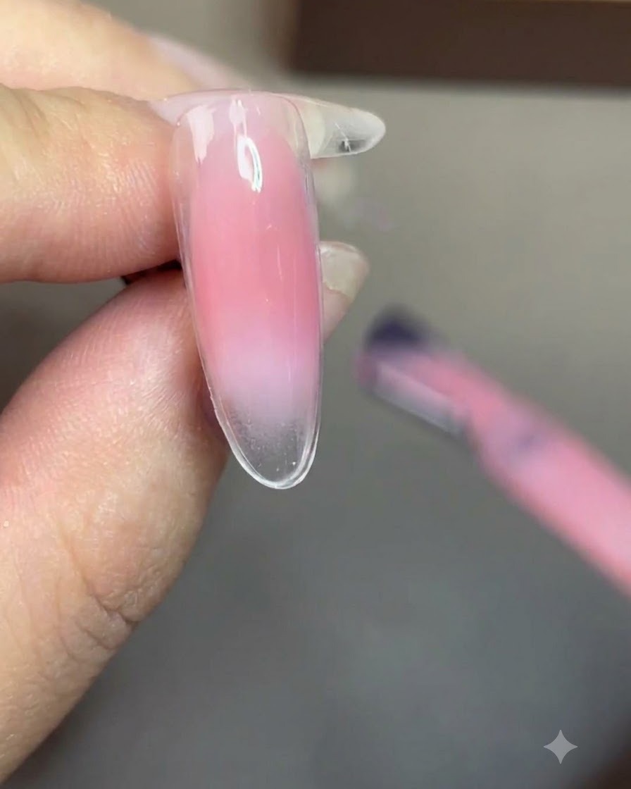 Un pincel aplicando esmalte de gel nude translúcido de manera uniforme sobre toda la uña.