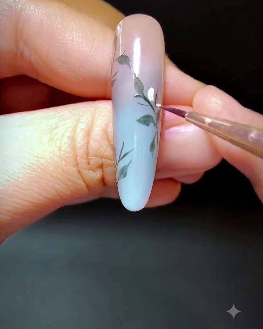 Primer plano de una uña decorada donde se aplican pequeños puntos de gel blanco a lo largo de la rama pintada.