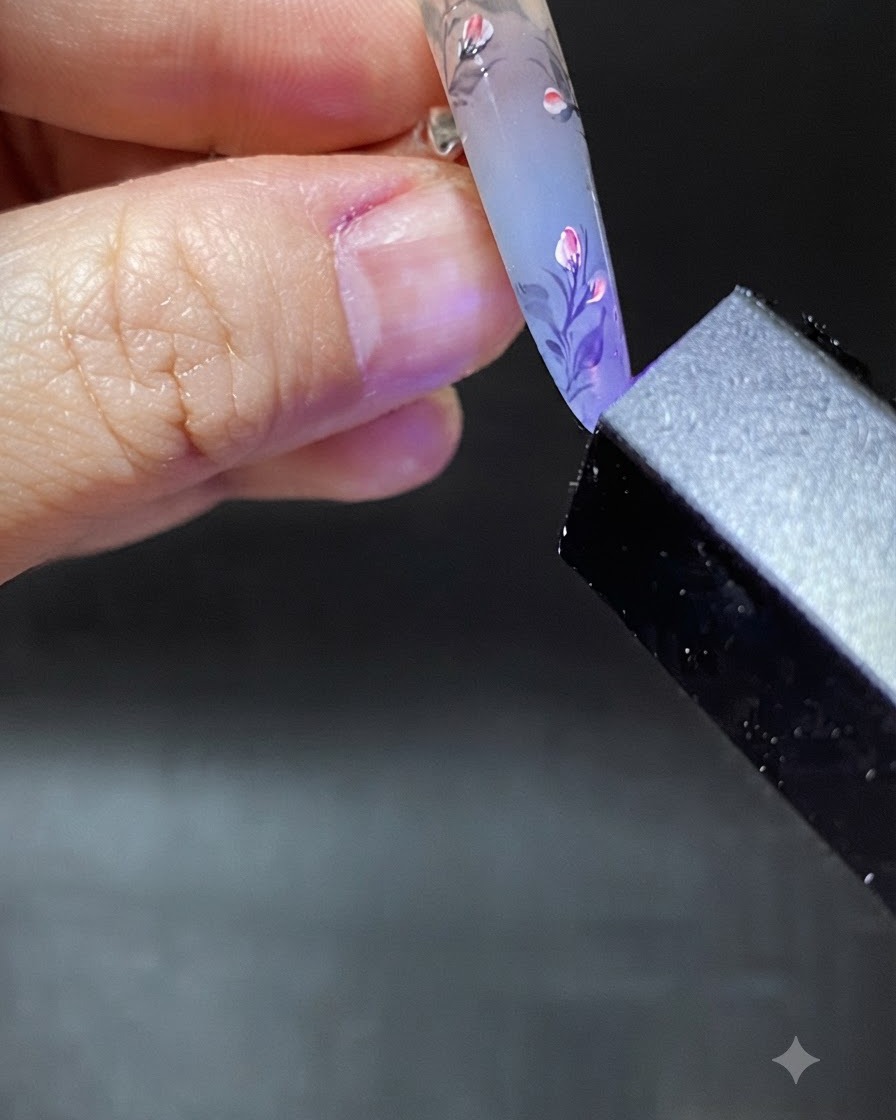 Un pincel aplicando una gota transparente de gel de refuerzo cerca de la zona de la cutícula de la uña decorada.