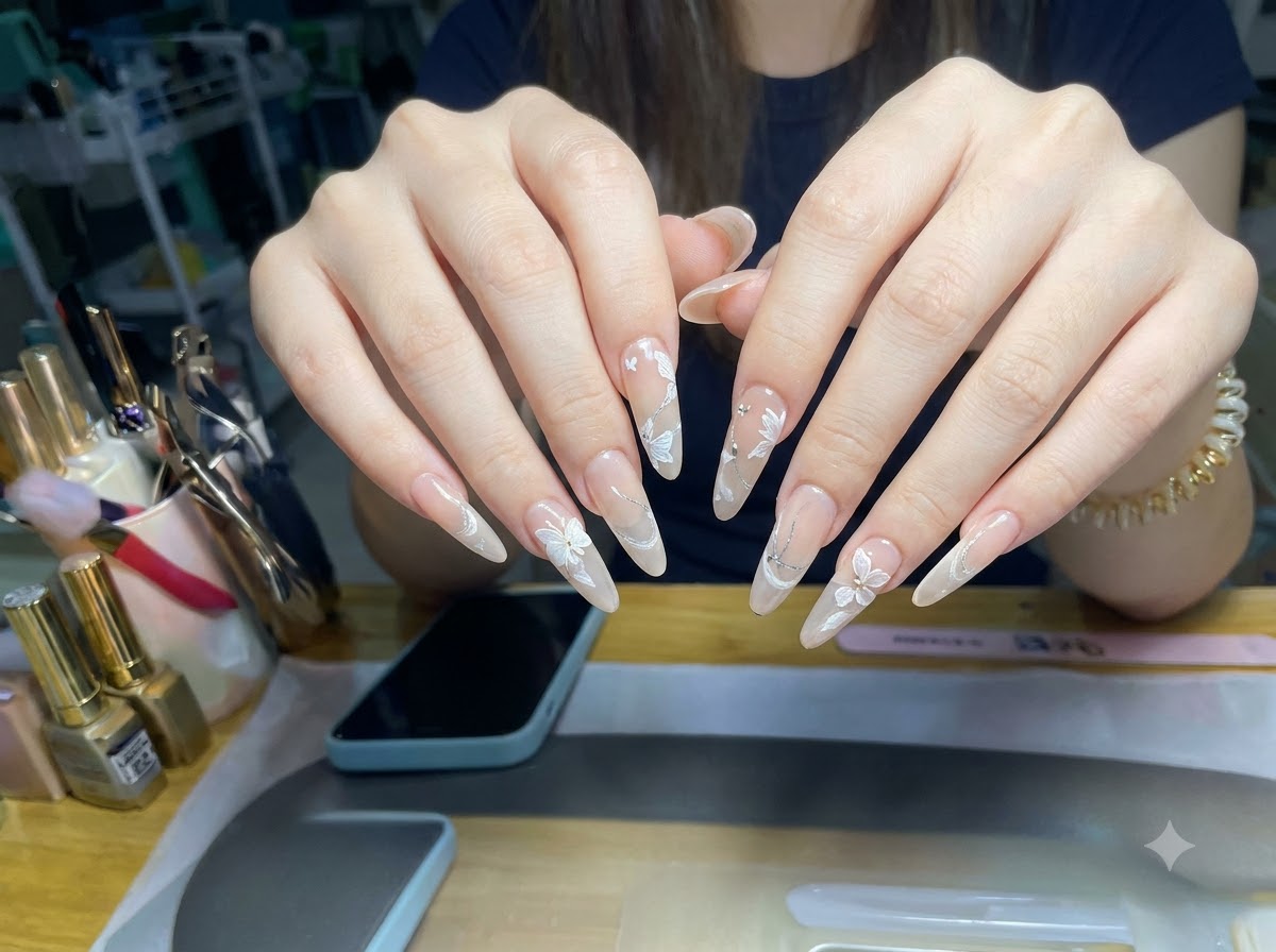 Un ángulo con macroenfoque que muestra la capa de purpurina de ojo de gato y los diseños florales en 3D en uñas con forma de almendra.
