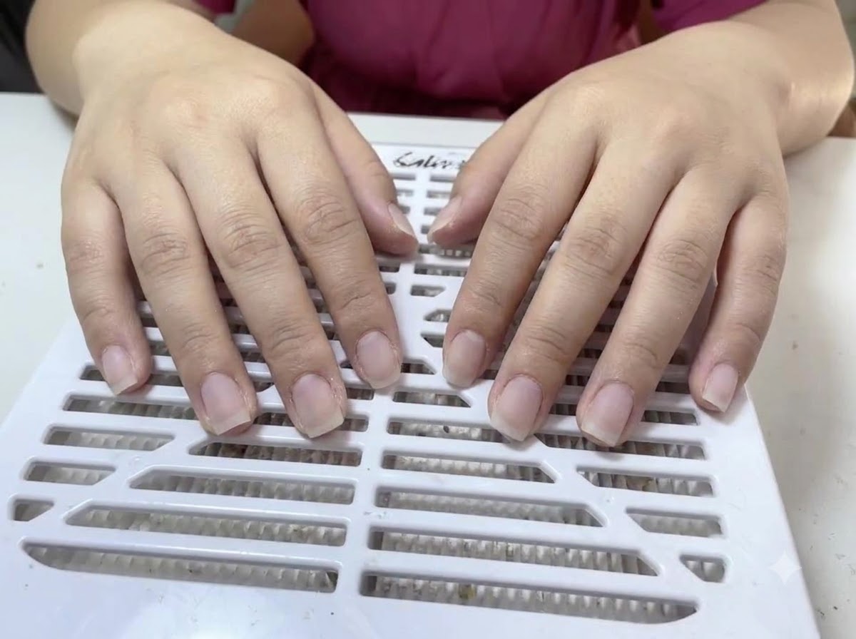 Dos manos con uñas naturales sin esmalte apoyadas sobre la superficie blanca y ranurada de un colector de polvo.