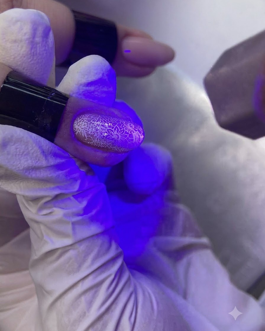 Una mano bajo una lámpara de uñas UV/LED morada curando una uña decorada.