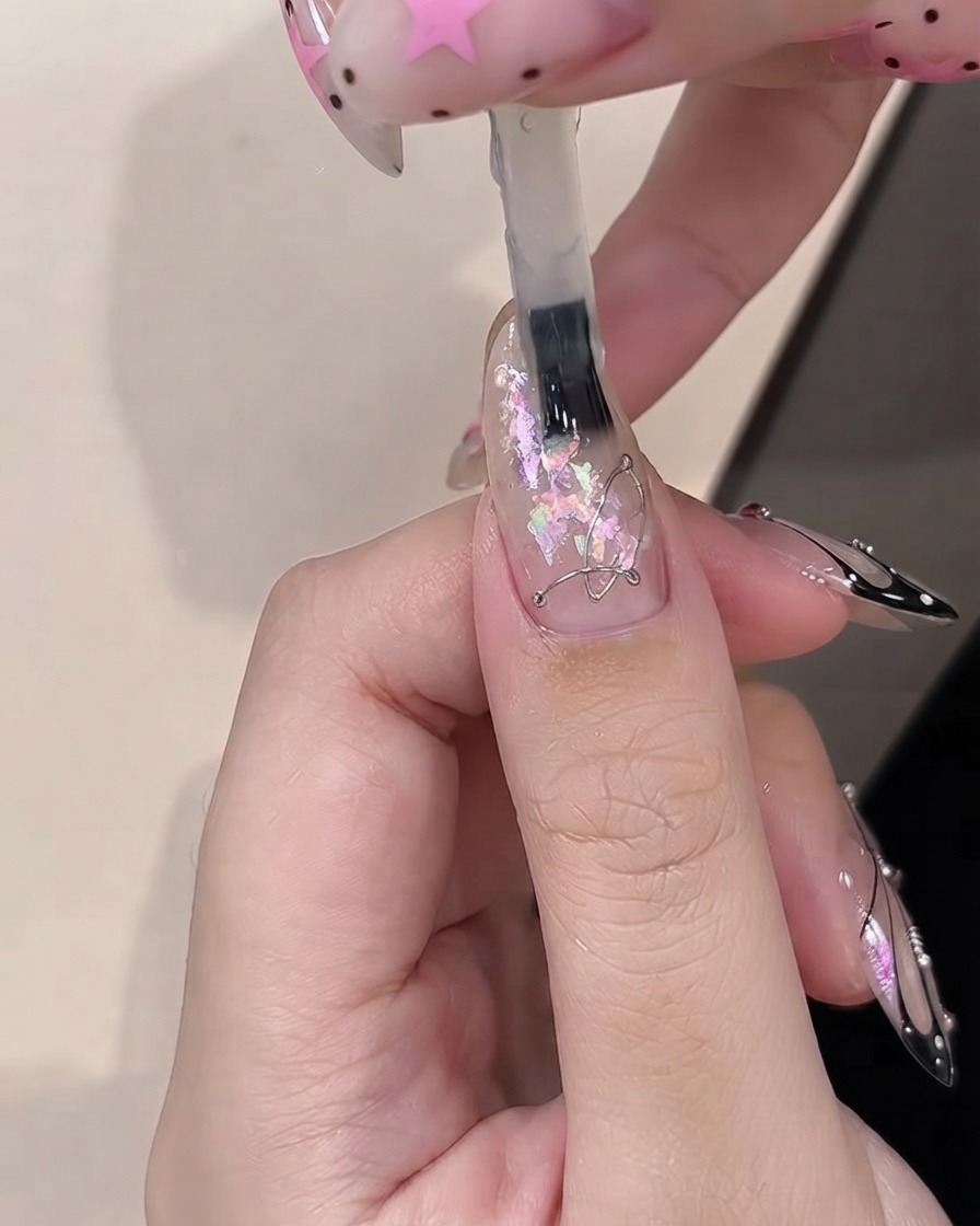 Un pincel aplicando gel constructor sobre piezas decorativas de ópalo incrustadas en una uña transparente.