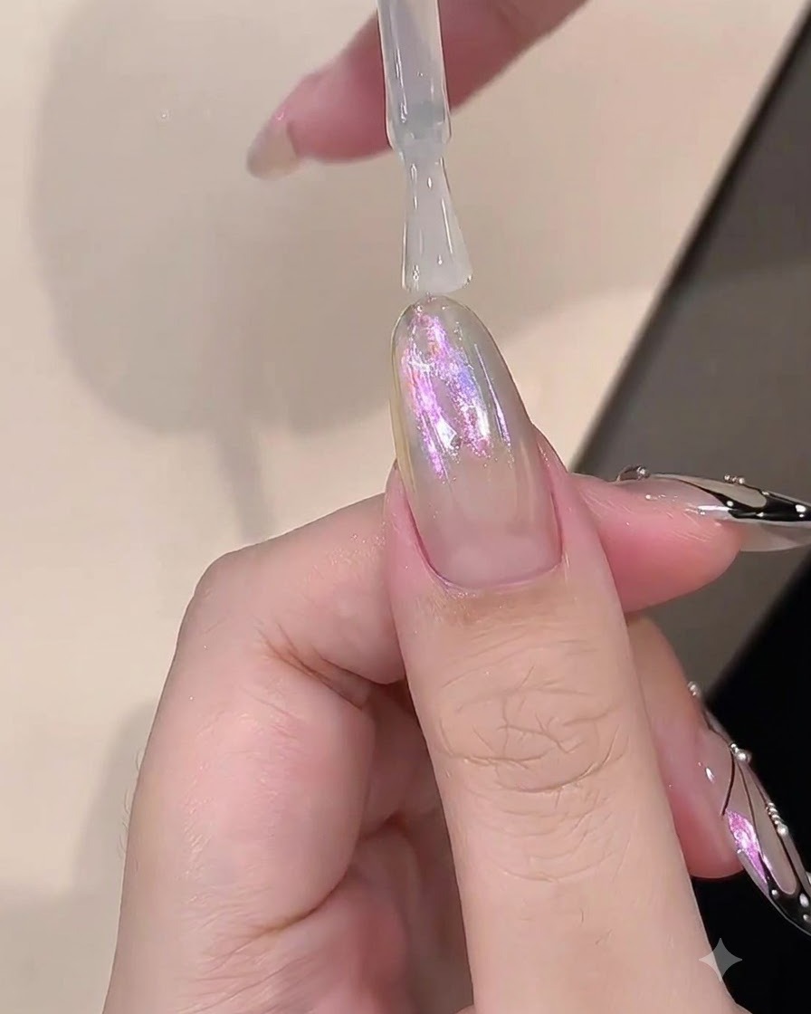 Un pincel aplicando una capa transparente de gel constructor sobre una uña con acabado cromado.