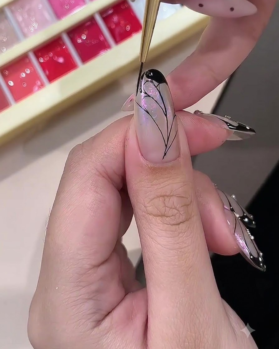 Una técnica de uñas rellenando los bordes exteriores de un diseño de ala de mariposa con gel negro opaco.