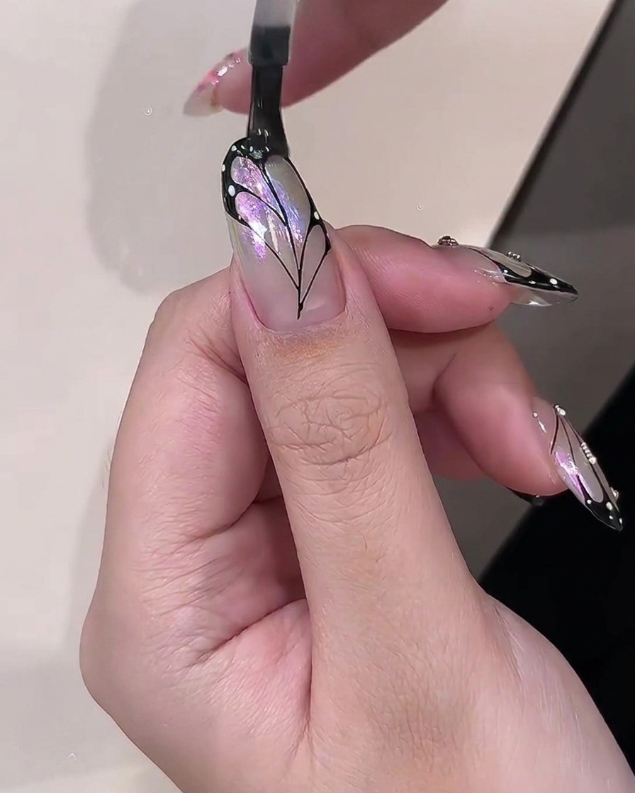 Un pincel aplicando un top coat transparente y brillante sobre un diseño de nail art de ala de mariposa terminado.