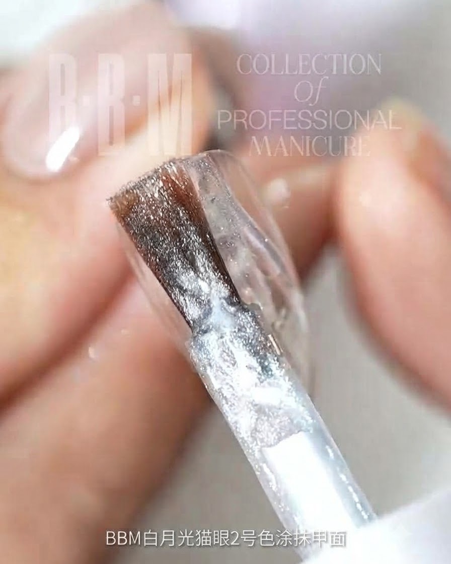Un pincel de uñas aplicando gel de ojo de gato con purpurina plateada sobre una superficie de uña transparente.
