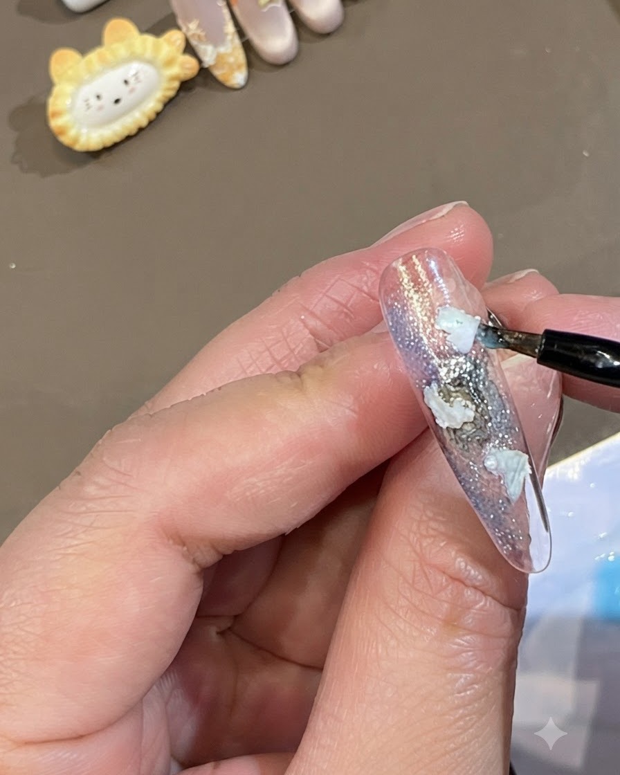 Un pincel fino colocando puntos de gel azul translúcido alrededor de los bordes de piezas de concha blanca en una uña.