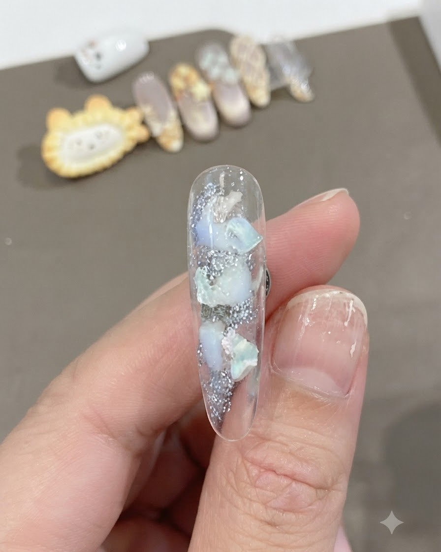 Un primer plano de una uña larga transparente con piezas de concha incrustadas y textura brillante con una mezcla suave de degradado blanco.