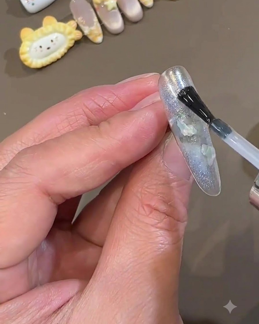 Un pincel de esmalte aplicando una capa lisa de capa superior transparente sobre una uña press-on azul hielo encapsulada.