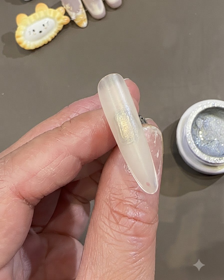 Un primer plano de una mano sosteniendo una punta de uña esmerilada preparada con un parche rectangular de gel deslizante transparente aplicado en el centro.