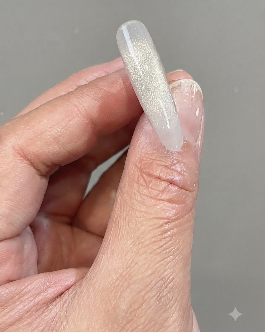 Una mano sosteniendo una punta de uña transparente que presenta un degradado vertical brillante hecho de gel reflectante de diamante agrietado.