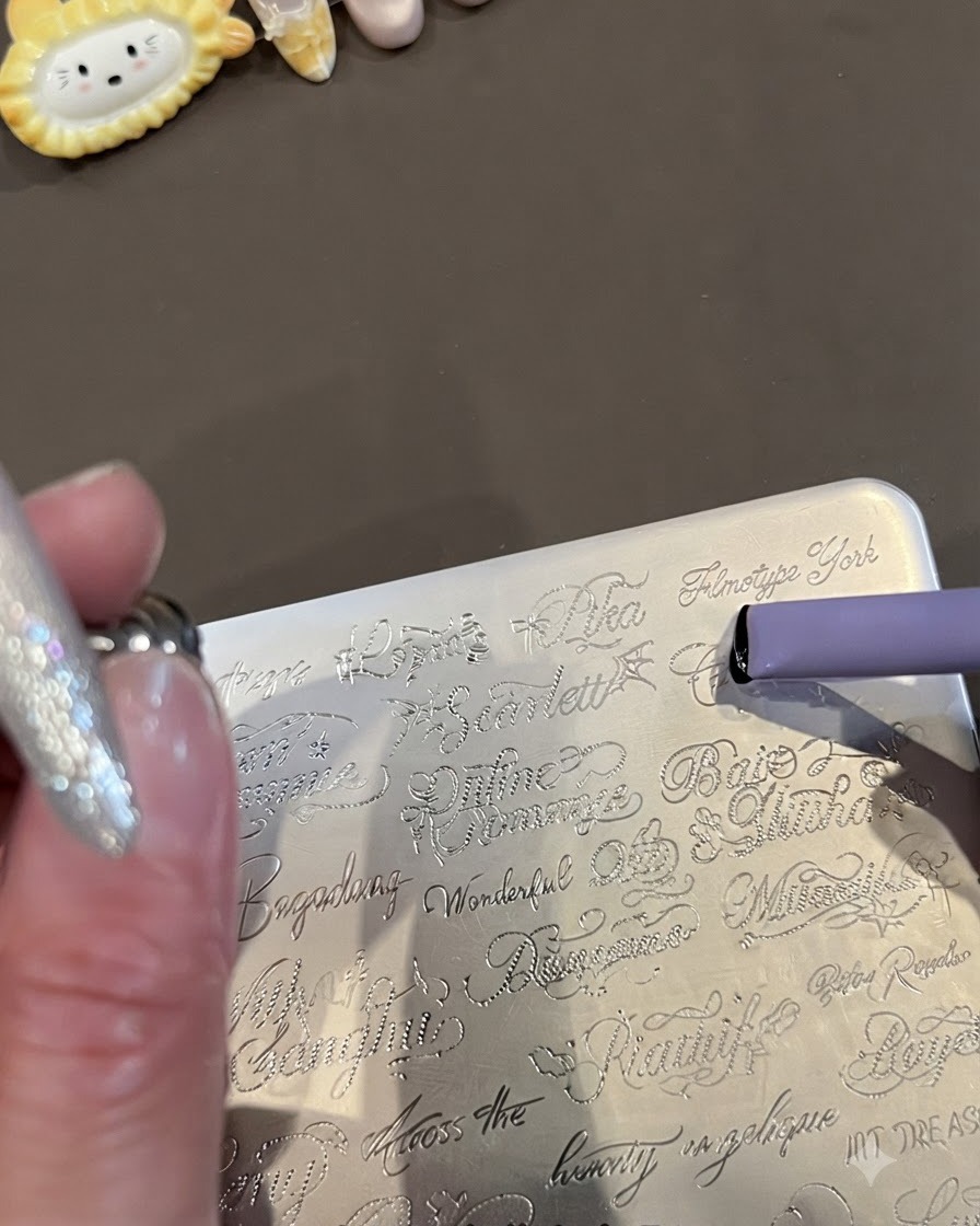 Un primer plano de una placa de estampación de metal grabada con palabras cursivas en inglés y un sello de gelatina morado que recoge el diseño.