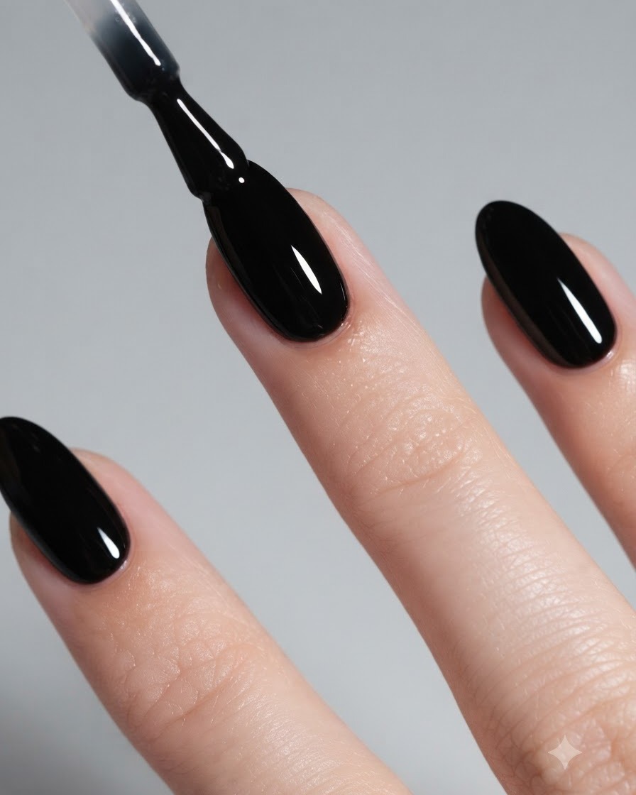 Primer plano de un pincel aplicando esmalte en gel negro brillante sobre una uña almendrada.