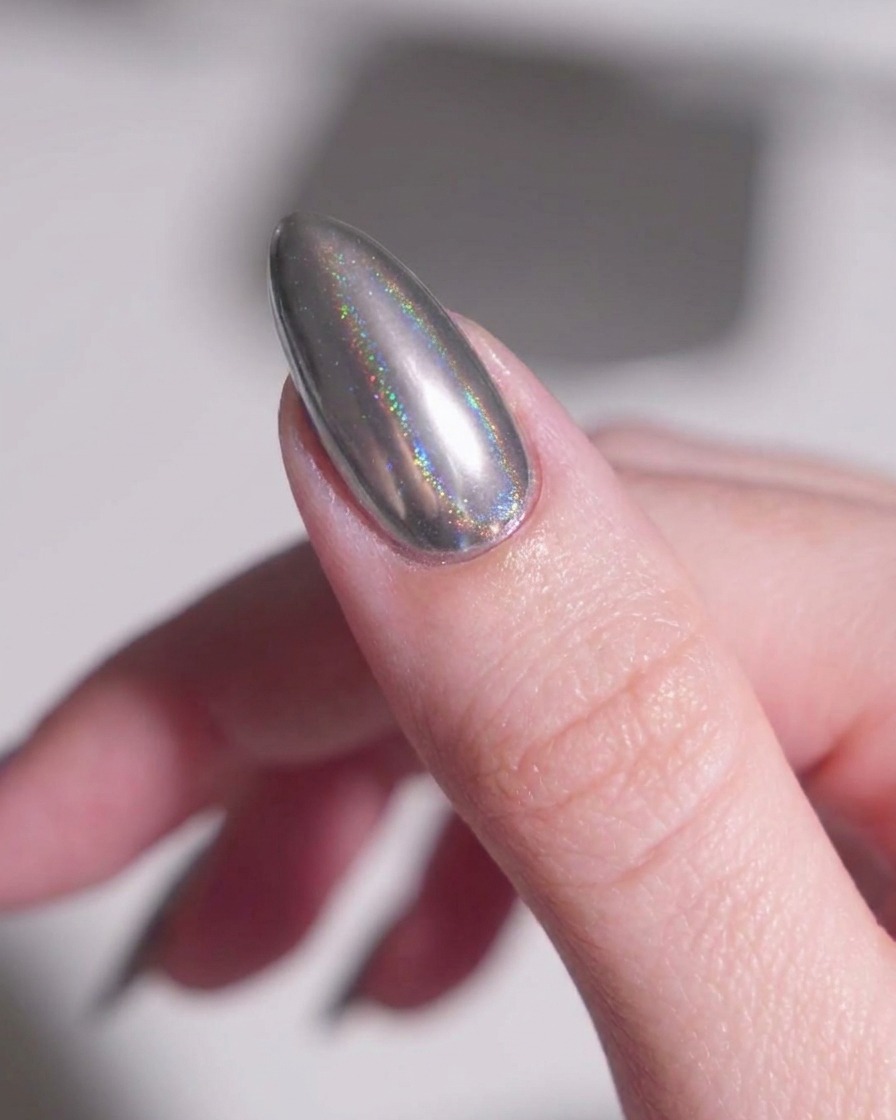 Una brocha de maquillaje suave limpiando el polvo plateado metálico suelto de la piel alrededor de una uña cromada.