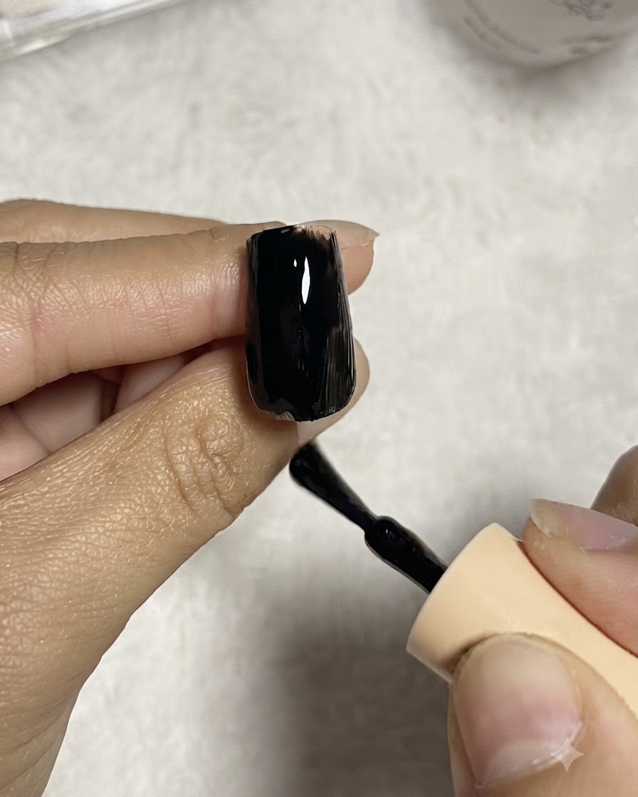 Un pincel de uñas aplicando una capa uniforme de esmalte en gel negro sobre una extensión de uña transparente.